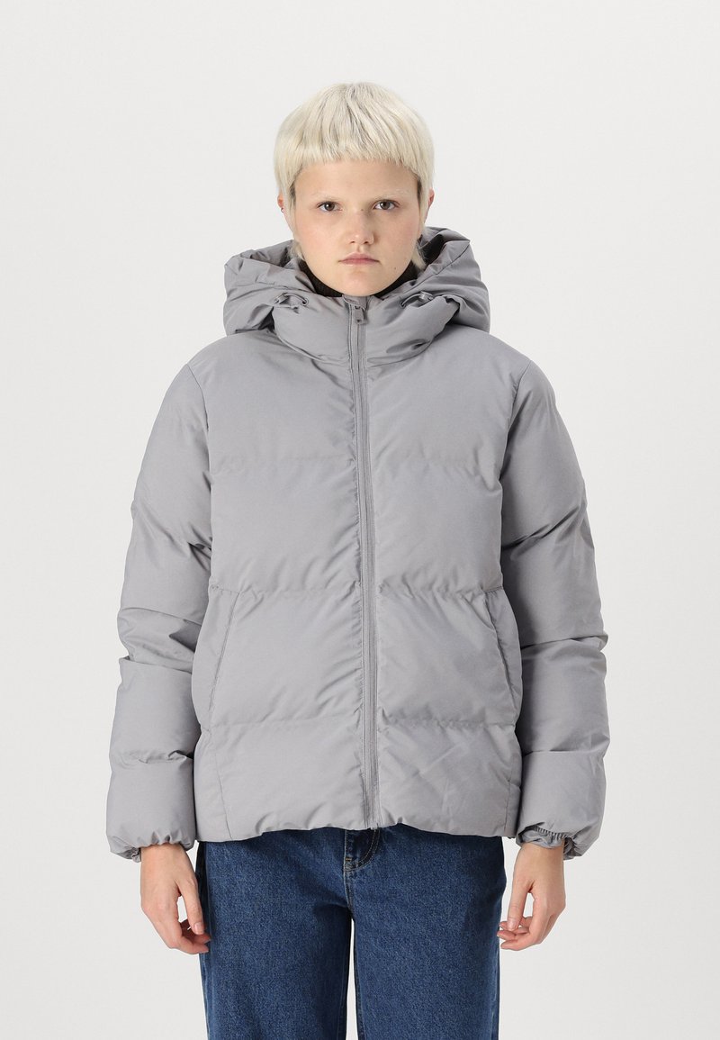 Grå puffjacka med huva, som har en framdragkedja, elastiska ärmslut och fluffig isolering. Bärs med blå jeans. Minimalistisk design.