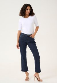 Jean bleu foncé avec une coupe droite, taille mi-haute et deux poches avant. Associé à un haut ajusté à manches courtes blanc.
