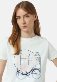 T-shirt en coton blanc avec un graphique de vélo en bleu et rose, et le texte "IDENTITÉ CASUAL FONDÉE EN 2010" en noir. Manches courtes.