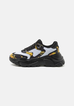 Sneaker in bianco e nero con materiali in rete e sintetici lisci. Presentano accenti gialli, una suola spessa e occhielli rotondi.