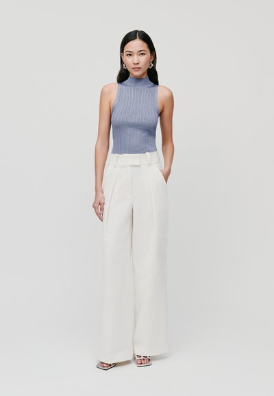Mouwloze ribgebreide top in lichtblauw, gecombineerd met hoge witte wijde broek met een ceintuur in de taille. Zilveren enkellaarsjes met bandjes.