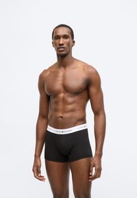 Sorte boksershorts med en hvid linning, der har "Tommy Hilfiger"-logoet. Stoffet virker glat med et tætsiddende design.