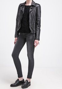 Chaqueta de motociclista de cuero negro sobre un suéter negro texturizado, combinada con jeans ajustados oscuros y zapatos negros robustos.