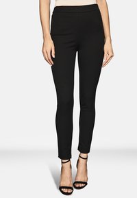 Svarta tajta byxor med en slät textur och hög midja. Har två sidofickor och en kortad fåll, tillsammans med svarta remsandaler.