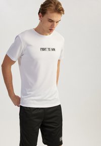 Witte sport T-shirt met korte mouwen, met een zwart "FIGHT TO WIN" tekstontwerp in het midden. Materiaal lijkt soepel en lichtgewicht.