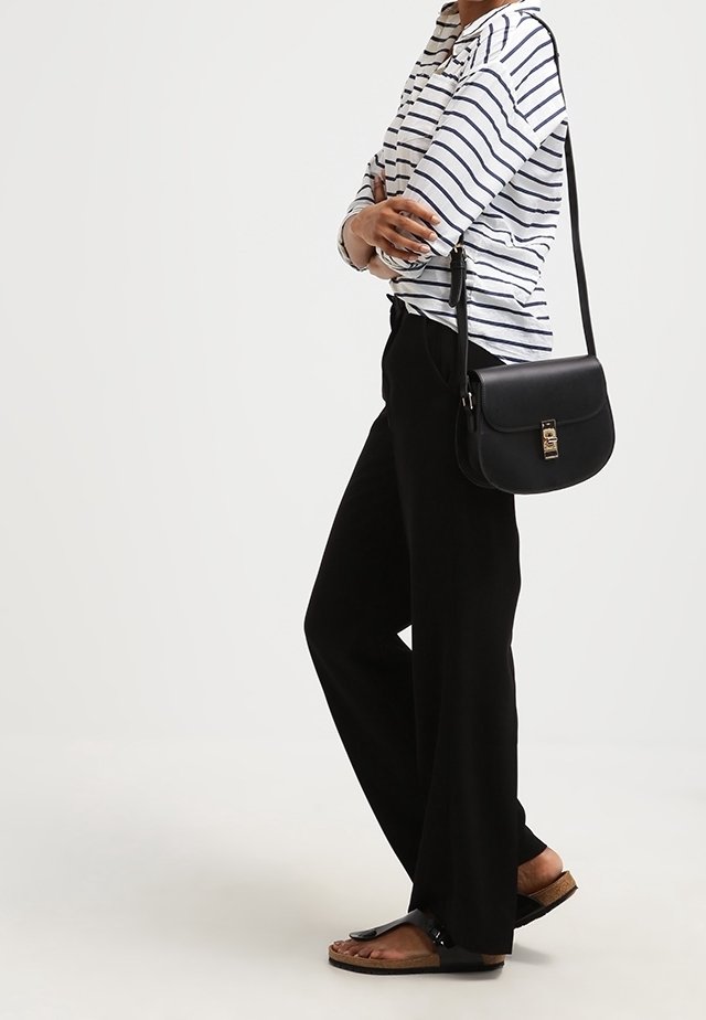 Pantaloni neri a gamba larga abbinati a una camicia a maniche lunghe a righe bianche e blu. Una borsa a tracolla nera con chiusura dorata e sandali piatti.