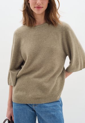 Beige knit sweater with a crew neckline and short, loose sleeves. Soft texture; paired with blue denim jeans. Minimalist design.