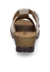 White leather sandal with a brown textured sole, open back, and adjustable strap. The insole is padded for comfort.