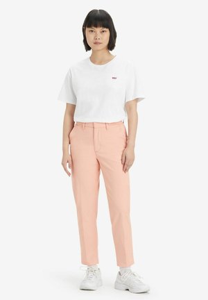 White cotton t-shirt with small red logo, paired with light pink straight-leg trousers, worn with white sneakers. Simple and clean design.