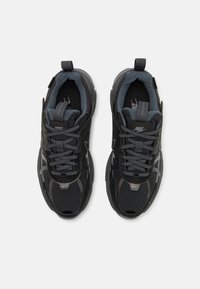 Melnas sporta kedas ar gludu un faktūru materiālu miksi, iekļaujot pelēkas akcentus, biezas zoles un kontrastējošas šņorītes.