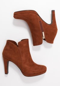 Stivaletti in suede marrone con tacco alto e cerniera laterale, caratterizzati da una punta arrotondata e dettagli cuciti lungo le cuciture.