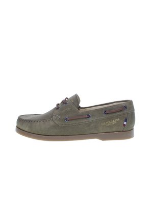 Zapato de barco de ante verde con cordones y ojales marrones, presenta una puntera cosida y suela de cuero. Logotipo de "U.S. Polo Assn." visible en el lateral.