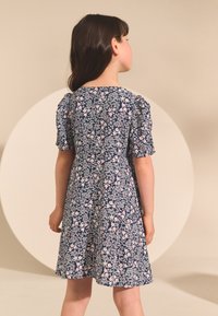 Laivastonsininen kukkainen mekko, jossa on lyhyet puffhihat, pinkin ja valkoisen kukkakuviointi, levenevä helma ja pyöreä pääntie.