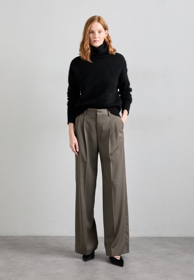 Black turtleneck sweater in a soft fabric, paired with high-waisted, wide-leg olive trousers. The outfit is completed with black pointed-toe heels.
