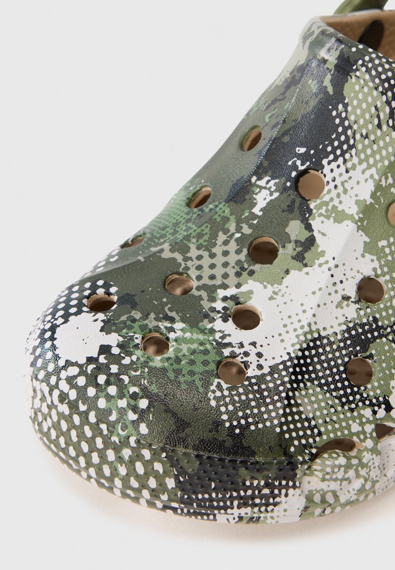 Zoccoli con motivo camouflage verde e bianco, realizzati in materiale leggero, dotati di numerosi fori di ventilazione e design a punta arrotondata.