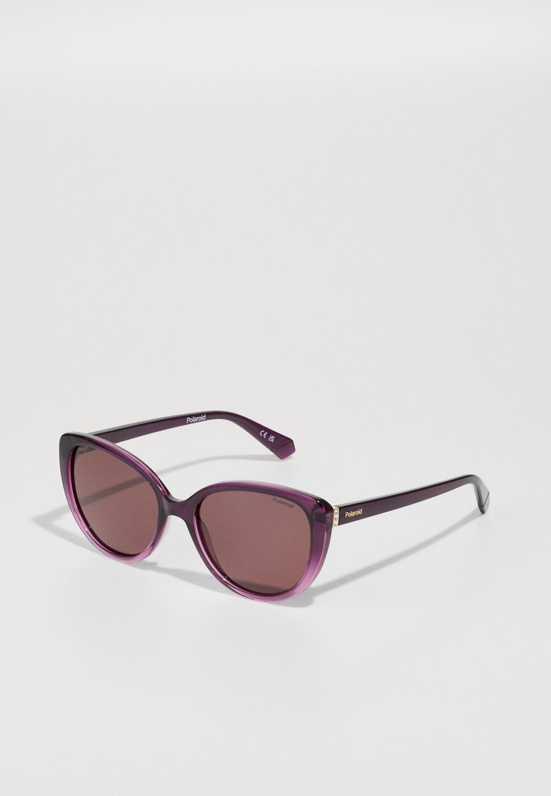 Lunettes de soleil cat-eye violettes avec verres dégradés, monture épaisse en plastique et détails dorés sur les branches. Texture lisse et brillante.