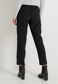 Pantalones elásticos negros con un ajuste relajado, cinturilla elástica y dos bolsillos traseros. Combinados con botines negros de tacón.