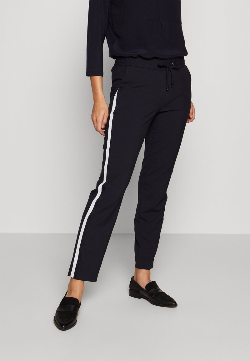 Marineblauwe broek met elastische taille, witte zijkanten, rechte pasvorm en trekkoord. Gecombineerd met zwarte loafers. Soepele textuur, casual ontwerp.