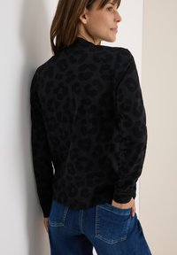 T-shirt noir à manches longues avec un motif léopard texturé. Le tissu semble doux, avec un col rond et une coupe décontractée.