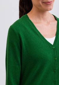 Grön cardigan i mjukt tyg, med V-hals, långa ärmar och fem knappar framtill. Slät textur med enfärgad design.