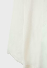 Biały materiał ułożony pionowo, ukazujący miękką teksturę i staranne szwy wzdłuż dolnej krawędzi.