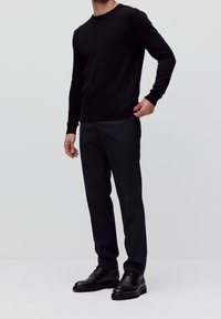 Maglione nero a girocollo, abbinato a pantaloni scuri sartoriali e stivali eleganti neri. Texture liscia e design aderente per un aspetto snello.