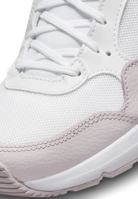 Basket blanche en matériaux maillés et en cuir, avec une touche rose texturée, un embout rond et des lacets blancs. Détail de couture notable.