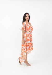 Blumenkleid mit orangenem Grundton, leichten blauen und weißen Blumen, kurzen Rüschelärmeln, einem V-Ausschnitt und einem asymmetrischen Saum.
