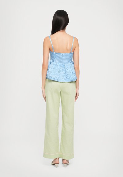 Top peplum brodat de culoare albastru deschis, cu curele subțiri, asortat cu pantaloni largi de culoare verde deschis cu detalii roz la tiv și o textură fină.
