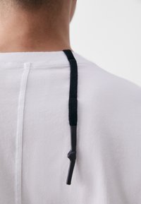 Fehér ing, hátul fekete zsinórral és texturált felülettel. Letisztult, egyszerű vonalak és minimalista dizájn.