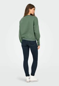 Groene, oversized sweatshirt met een ronde hals, gecombineerd met donkere skinny jeans en witte high-top sneakers.