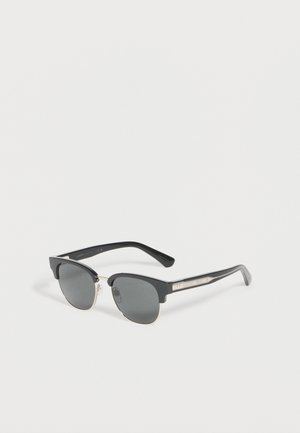 Occhiali da sole semirilievi neri e argento con lenti scure, aste curve e naselli su sfondo bianco.