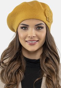 Mosterdgele wollen baret met een gemêleerde afwerking, voorzien van drie stoffen rozenaccenten aan de zijkant en een zachte, afgeronde vorm.