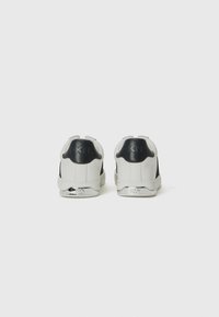 Sneakers bianchi in pelle con dettagli neri, caratterizzati da una texture liscia, forma arrotondata, collo imbottito e dettaglio logo metallico sul tallone.