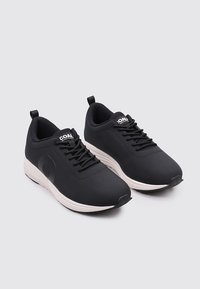 Zapatillas deportivas negras con parte superior de textil suave, puntera redonda, diseño con cordones y una mediasuela blanca. Sin patrones visibles, estilo minimalista.