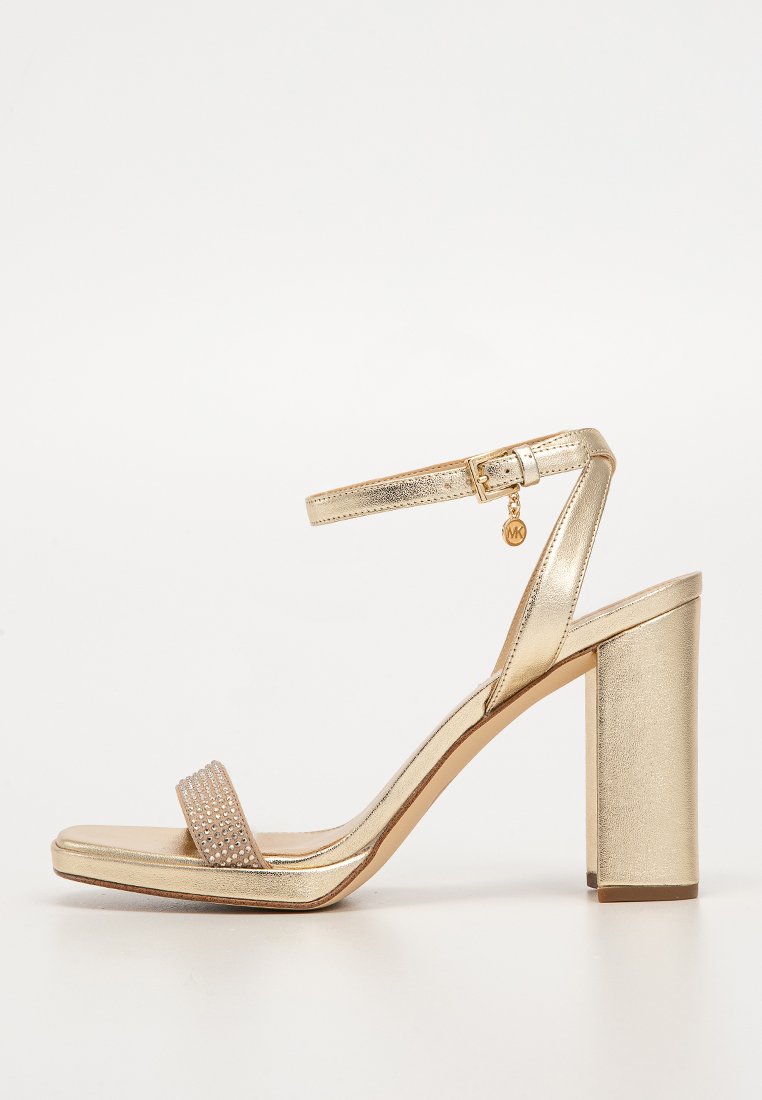 Sandale à talons hauts dorée avec un large talon bloc, présentant une finition métallique lisse, une fine sangle autour de la cheville et une bande ornée de strass.