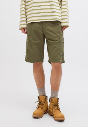 Shorts cargo en coton vert olive, dotés de poches latérales, coupe droite, associés à des bottes beiges et des chaussettes grises. Haut à rayures horizontales à manches longues.
