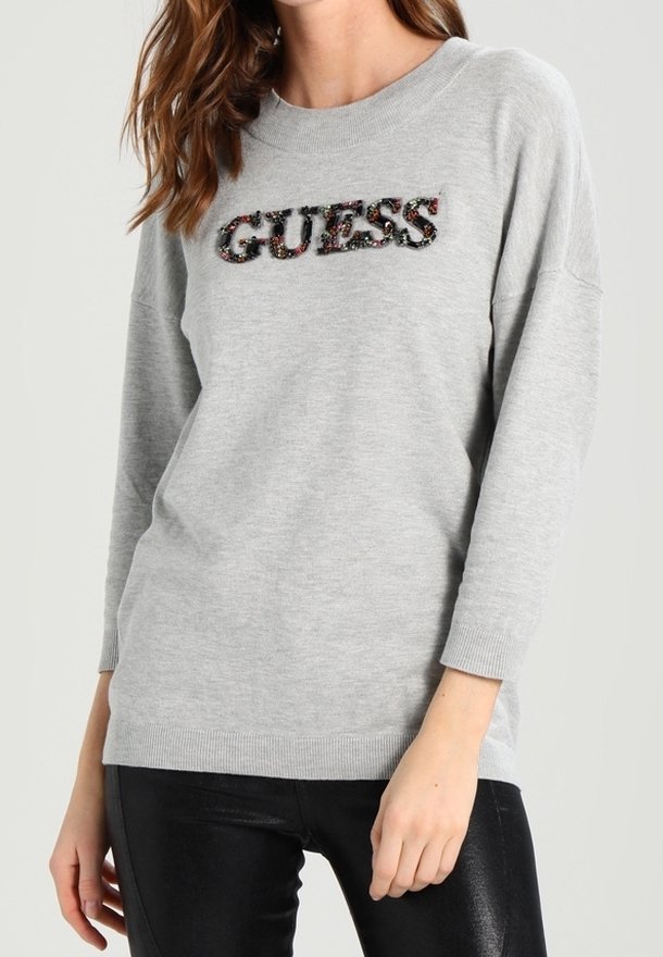 Šedá mikina oversized střihu s nápisem "GUESS" v dekorativních aplikacích na prsou. Hranaté manžety a spodní lem.