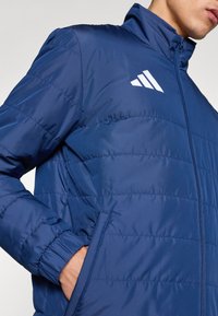 Μπουφάν navy με φερμουάρ, με οριζόντιες ραφές και λευκό λογότυπο στο αριστερό στήθος. Υλικό με υφή, ελαφρύ.