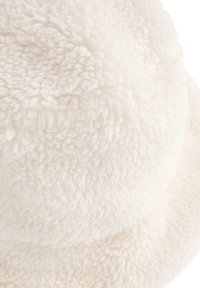 Krem kapa od mekog, teksturiranog umjetnog krzna; ima zaobljen vrh i široki, ravni rub.