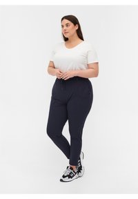 Weißes kurzärmliges T-Shirt kombiniert mit marineblauen Sport-Jogginghosen mit Kordelzug, tailliertem Schnitt und schwarzen Sneakers mit weißen Akzenten.