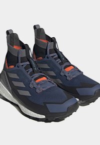 Marineblaue und schwarze Sportschuhe mit texturiertem Strickobermaterial, orangen Akzenten, grauen Überzügen und weißer Dämpfung entlang der Sohle.