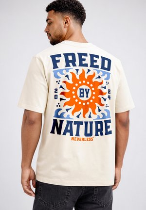 Man wearing cream t-shirt with large orange sun and text "FREED BY NATURE" in blue on back, paired with black jeans.
