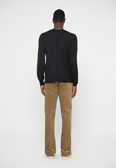Black knitted sweater with long sleeves, featuring a central back seam. Paired with light brown corduroy pants and casual footwear.