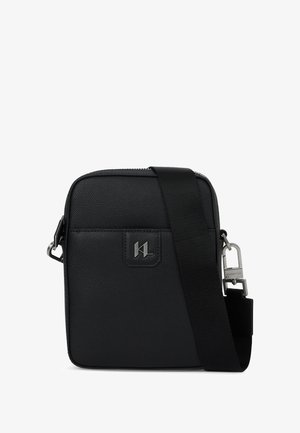 Čierna crossbody taška s textúrou, striebornou logovou plaketou, nastaviteľným čiernym popruhom a strieborným kovaním, zobrazená na bielom pozadí.
