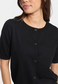 Svart kortärmad cardigan med rund halsringning, med en knappslå framtill och ribbade detaljer, gjord av ett mjukt trikåmaterial.
