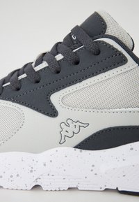Gray and white athletic shoe with mesh panels, textured accents, and a speckled white sole. Features gray laces and a logo.