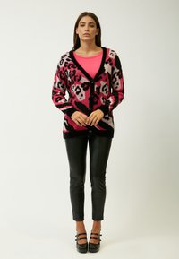 Leopardprint cardigan in roze, zwart en wit, met lange mouwen, een V-hals en knoopsluiting, gecombineerd met zwarte neplederen broek.
