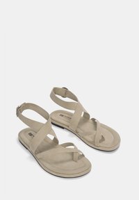 Beige platte sandalen met kruislings gespen en enkelgesp. Gladde suede-achtige textuur, gevormde voetbed en dunne zwarte rubberen zool.