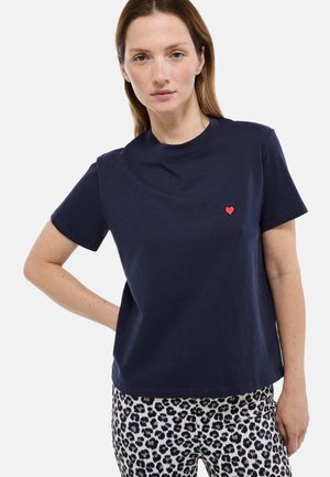 T-shirt en coton bleu marine à manches courtes, col rond, avec un petit motif de cœur rouge sur la poitrine gauche.